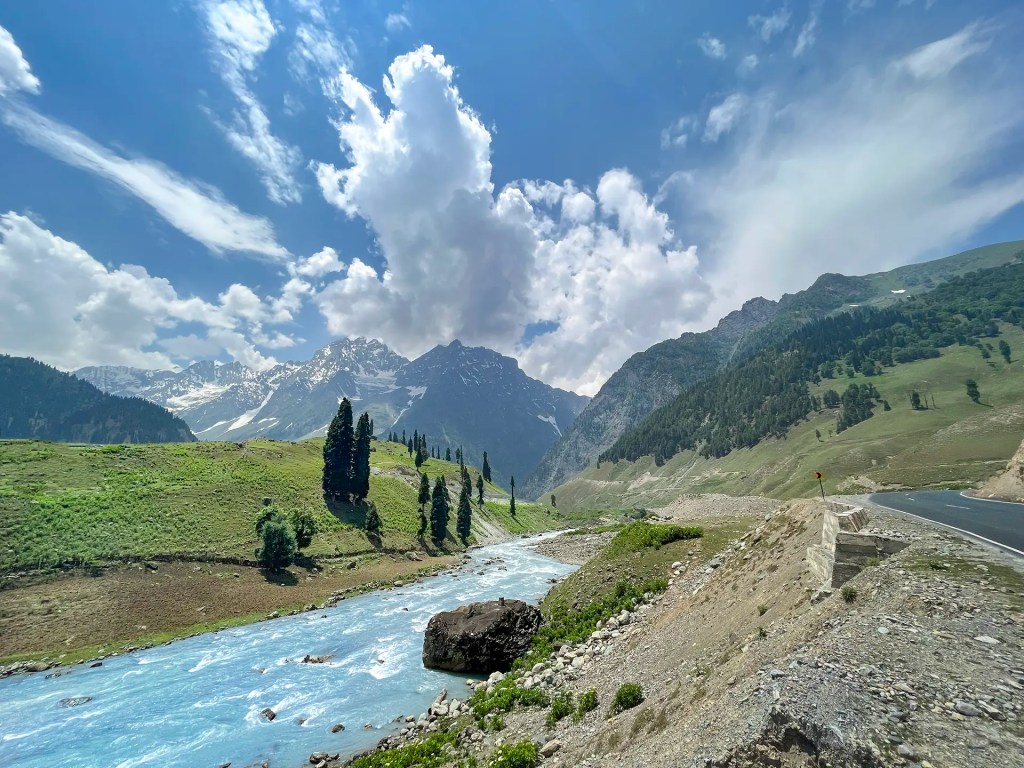 Glacial river flowing through green valley with mountains and clouds near Sonmarg Kashmir