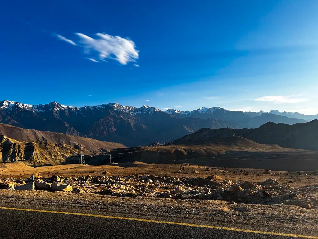 Arid hills and distant snow capped mountains on outskirts of Leh Ladakh under blue sky