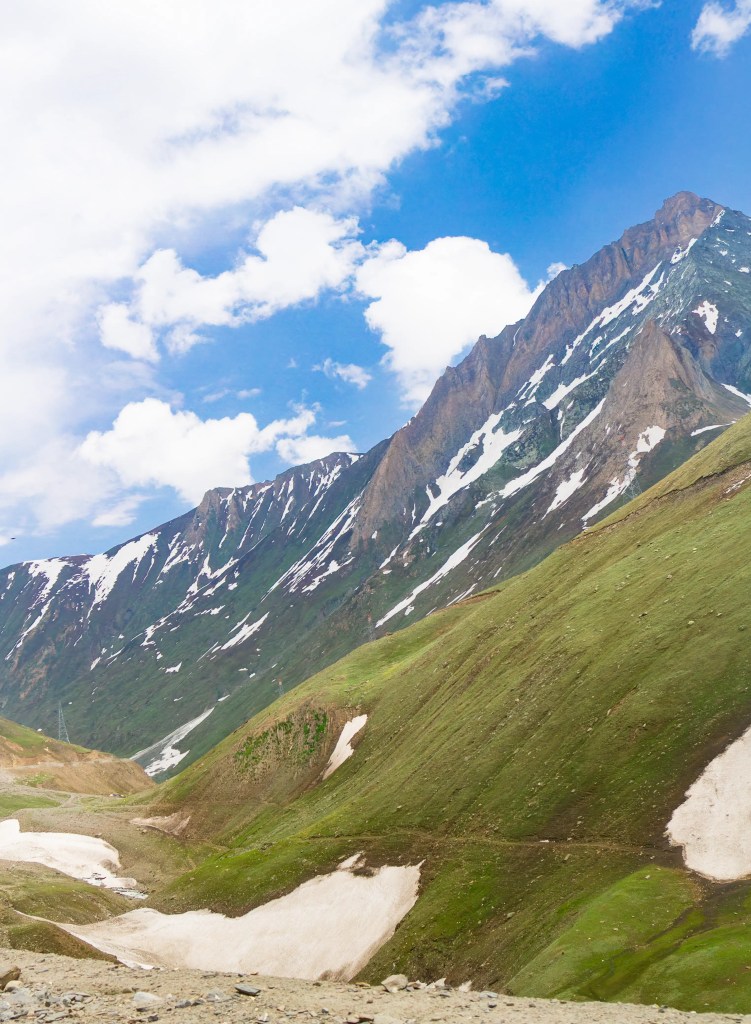 Snow-streaked mountain ridges with green slopes under a blue sky across Zoji La Ladakh